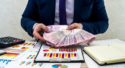 young businessman in office counts money as profit after a successful deal. The man compares and...