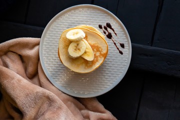Closeup of delicious pancakes, with banana and chocolate on a dark background. View from above.
