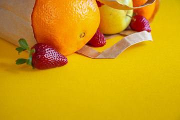 Healthy tasty food. The most delicious and juicy fruits. Strawberries, oranges, tangerines, apples are a great set for a fruit salad. A paper bag with fruits licks on a yellow background.
