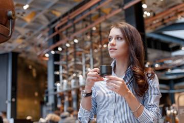 Young beautiful girl in a cafe with a coffee mug in a black cup, looks away.