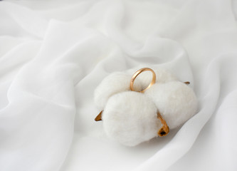 Fototapeta na wymiar Elegant wedding concept. Golden ring with cotton flower pillow on white silk background. Feminine still life composition. Minimalist style. Copyspace.