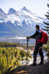 Hiking in Canadian Rockies. Adventurous man overlooking beautiful mountain landscape and The Three Sisters Peaks in Canmore, Alberta, Canada 