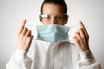 Woman in white protective suit and goggles puts on medical mask