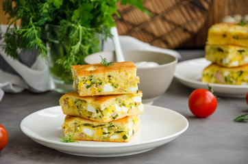 Pieces of homemade pie with eggs, green onions and canned tuna on a white plate on a dark concrete background. Horizontal orientation.