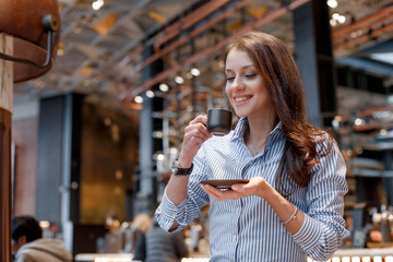 Fototapeta premium Young beautiful nice girl in a cafe smiles and looks at a cup of coffee.