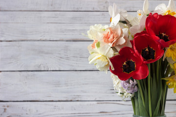 Bouquet of beautiful daffodils of different types, red tulips and hyacinths on a white wooden background