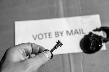 Hand holding a key in front of envelope for vote by mail ballot depicting the key to election security.  Selective focus