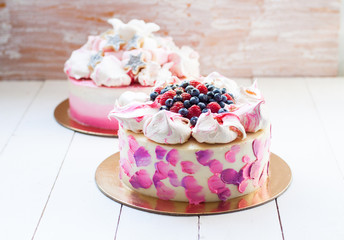 White and pink birhday cake with meringues and fresh berries, raspberries, strawberries and blueberries.