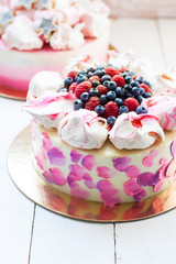 White and pink birhday cake with meringues and fresh berries, raspberries, strawberries and blueberries.