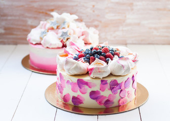 White and pink birhday cake with meringues and fresh berries, raspberries, strawberries and blueberries.