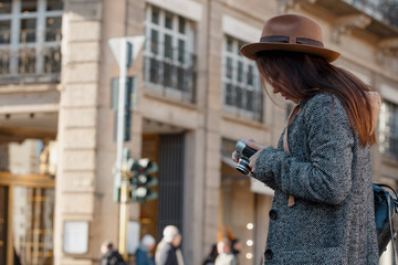 A beautiful young girl tourist holds a camera in his hands and looks at the screen to see the result of the shooting.