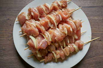 Close up Picture of raw chicken breast skewers with pieces of onion marinated in olive oil with greek style spices and herbs waiting on the white plate to be placed on charcoal grill.