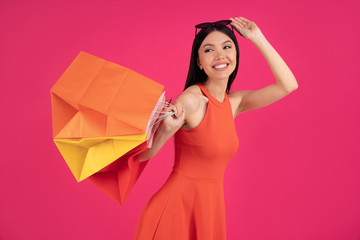 Obraz na płótnie Canvas Image of a beautiful shocked young brunette asian woman posing isolated over pink wall background holding shopping bags.