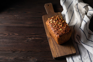 Homemade crusty loave of bread with pumpkin seeds on wooden background. Still life concept. Dark mood