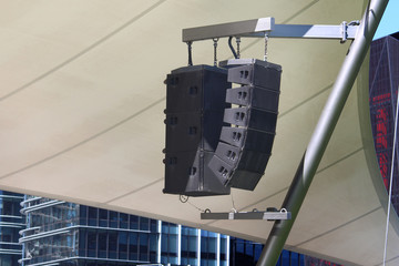 Black commercial outdoor speakers suspended from a metal pole they are servicing an outdoor theatre...