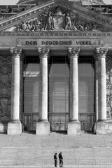 Facade of Reichstag building from 1894, home of German federal parliament (German Deutscher Bundestag), with inscription “The German People” over columns. Security police guards walk by