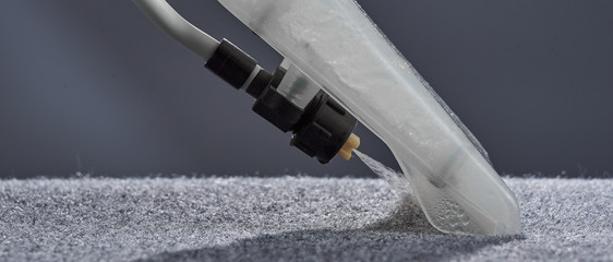 Washing carpet with vacuum cleaner close-up on gray background.