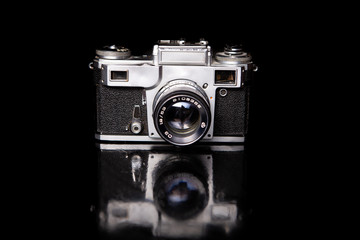 Old vintage camera is on a reflective surface on a black background