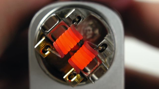 Vaping atomizer with clapton coil is working on a white background.