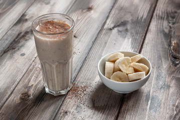 Ingredient for smoothies. Banana smoothie with cocoa in a transparent faceted glass on a wooden background. View from above