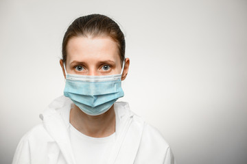 woman in medical mask and white protective suit looks at camera.