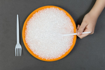 Plastic plate with recycled plastic pellets and fork with a spoon on a dark background, a person eats plastic pallets .Concept of environmental pollution with plastic