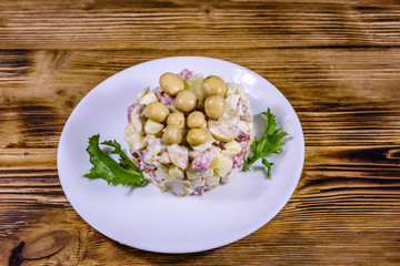 Salad with marinated mushrooms, sausage, onion, boiled potato and mayonnaise on a wooden table