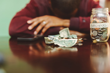african american  man at the table calculating how much he needs to tap into his savings or rainy day funds