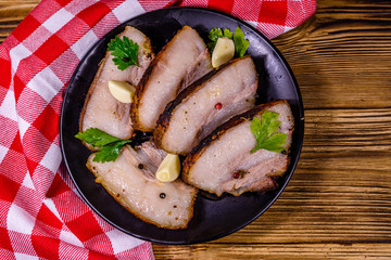 Slices of baked pork belly, garlic and parsley on a black plate. Top view