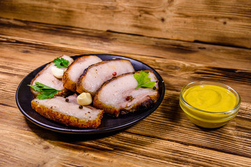 Slices of baked pork belly, garlic and parsley on a black plate