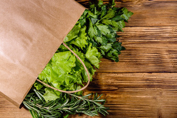 Paper bag with lettuce rosemary and parsley on a wooden table. Vegan food. Top view