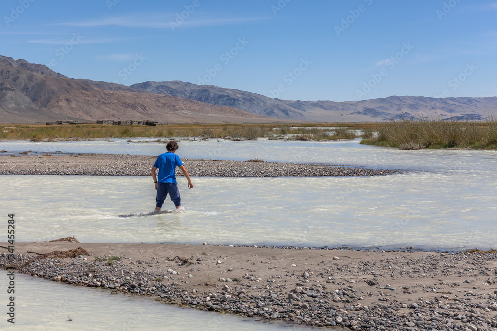 Wall mural man crosses a white mountain river on foot. altai, mongolia.