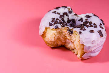 Bitten glazed donut with chocolate chip on top isolated on a pink background