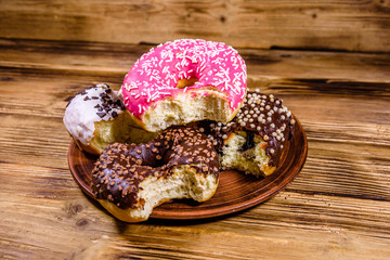 Plate with bitten glazed donuts on a wooden table