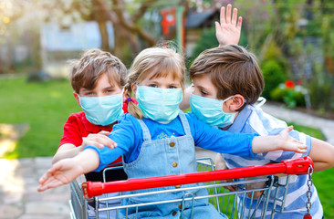 three kids, little toddler girl and two kid boys in medical mask as protection against pandemic coronavirus disease. Children with shopping cart using protective equipment as fight against covid 19.