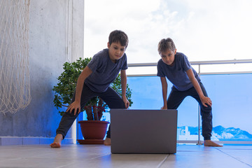 Children with laptop doing sport exercises at home on balcony. Sport, healhty lifestyle, active leisure, stay at home, online learning, online training