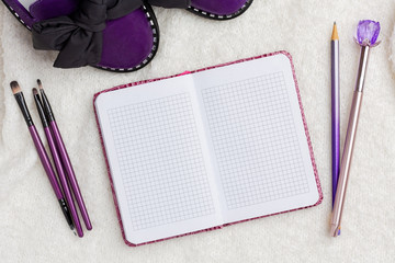 Notepad, purple women's shoes, eye brushes, pen and pencil lie on a white soft background.