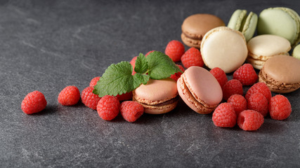Tasty french macarons with raspberries on dark stone background.