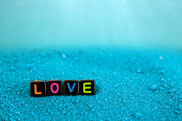 The word love is made up of colored letters on black cubes on blue sand underwater