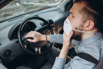 guy in a shirt and a medical mask sits at the wheel of a car. Precautions during the coronavirus epidemic. protect yourself COVID-19. Movement around the city in a pandemic.