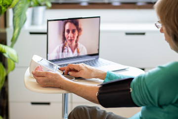 telemedicine concept elderly woman speaking to her doctor online and taking her blood pressure