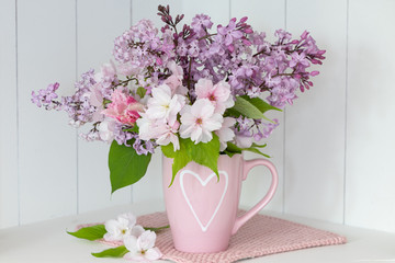Blumenstrauß mit Flieder und Zierapfel in Tasse mit Herzmotiv