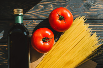 Products on the table. Pasta, olive oil in a bottle, tomatoes on a wooden background. Ingredients for cooking. Close-up