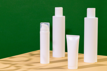 White plastic skincare tubes on a background of tropical plant shadow with copy space
