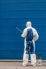 Man wearing an NBC personal protective equipment (ppe) suit, gloves, mask, cleaning the streets with a pressurized spray disinfectant water to remove covid-19 coronavirus. Concept of a pandemic.