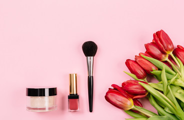 Obraz na płótnie Canvas Tools for applying light refreshing makeup lie on a pink background with a bouquet of red peonies. Bright spring-summer collection. Trendy background for advertising text.