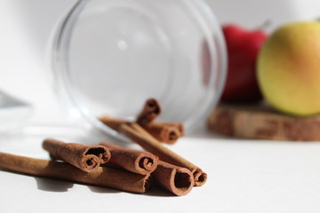 cinnamon sticks have fallen out of a glass jar apples are in the background yellow red green on a white background