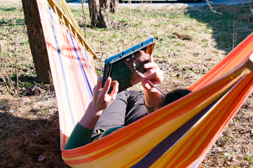 Girl works at home lying in a hammock on the backyard of her country house. Freelance concept. 