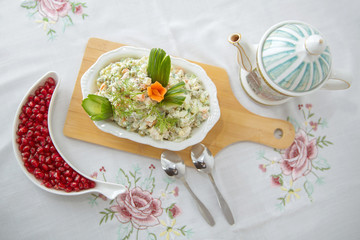 On the plate capital salad . Mayonnaise salad on a wooden board . Green peas, cucumber . Teapot . spoon . Granulated pomegranate . white tablecloth . Azerbaijani capital salad .