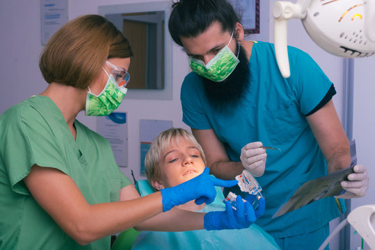 Young female and male dentists showing to their patient an X-ray picture of her teeth and a  prosthetic jaw